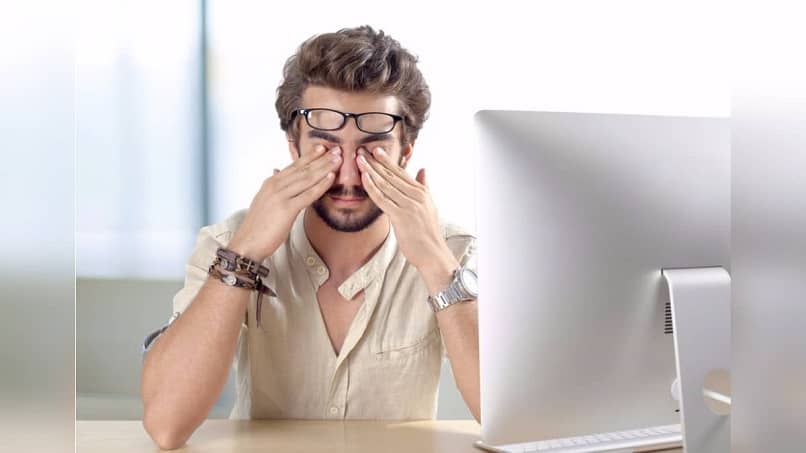 man covering eyes in front of computer